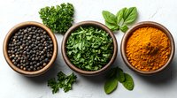Fresh aromatic spices and herbs in wooden bowls on light background - black peppercorns, chopped parsley and turmeric powder with basil leaves.