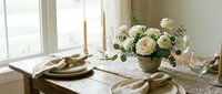 Elegant dining table setting with white roses centerpiece, candles, and neutral tableware creating sophisticated home decor atmosphere.
