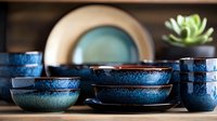Handcrafted ceramic bowls with deep blue reactive glaze finish stacked on wooden surface, featuring rustic pottery dinnerware with organic textures and patterns.