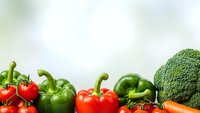 Fresh organic vegetables including red and green bell peppers, broccoli, cherry tomatoes and carrots arranged on white background for healthy cooking and nutrition.