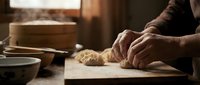 Baker hands kneading fresh dough on wooden surface in warm kitchen with natural lighting for artisan bread making and culinary preparation.