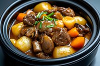 Hearty beef stew with tender meat chunks, baby potatoes, carrots in rich brown gravy sauce garnished with fresh chives served in black ceramic bowl.