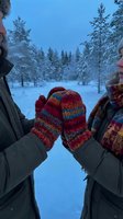Couple touching colorful knitted mittens in snowy winter forest at dusk, wearing warm jackets and scarves in cold weather outdoors.