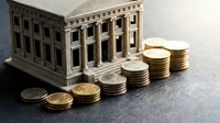 Miniature bank building model with stacked coins representing financial growth, investment planning, and economic stability concepts for business presentations.