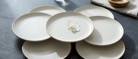Minimalist ceramic dinnerware set with cream-colored plates arranged on gray surface, featuring clean lines and modern design for contemporary table settings and home decor styling.
