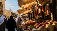 Traditional Middle Eastern spice market with vendors and customers browsing colorful displays of aromatic spices, dried fruits, and local products under fabric awnings.