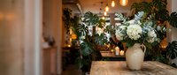 Cozy cafe interior with fresh white flowers in ceramic vase on wooden table, warm ambient lighting and green plants creating inviting atmosphere for dining.
