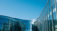 Modern curved glass office building facade with reflective windows against clear blue sky for corporate architecture and business concepts.