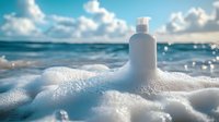 White cosmetic bottle in sea foam waves against turquoise ocean horizon and cloudy sky. Natural skincare and beauty product photography with beach atmosphere.