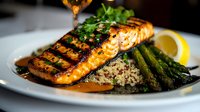 Grilled salmon fillet with grill marks served on quinoa pilaf and asparagus spears, garnished with fresh herbs and lemon slice in honey glaze sauce.