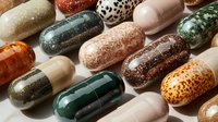 Colorful collection of decorative capsules and pills with various patterns, textures and finishes scattered on neutral background for medical design.