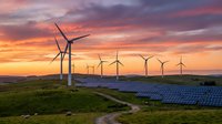 Wind turbines and solar panels generating renewable energy at sunset with dramatic orange and purple sky over green landscape creating sustainable power solution.