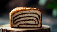 Freshly baked layered bread with chocolate swirl pattern shown in cross section on wooden board. Close up macro shot with soft natural lighting and blurred background.