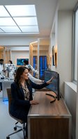 Professional businesswoman analyzing data on computer screen in modern office environment with colleagues working in background laboratory setting.