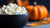 Fresh popcorn in black ceramic bowl with autumn pumpkins and fall leaves creating seasonal Halloween or Thanksgiving mood on dark background.