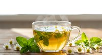 Steaming hot herbal tea in glass cup with fresh mint leaves and chamomile flowers on wooden table for relaxation and wellness.