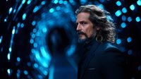 Middle-aged Caucasian man with long dark hair and beard wearing black suit against dramatic blue bokeh lights background, profile view creating mysterious atmosphere.