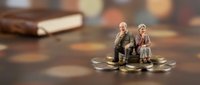 Miniature elderly couple sitting on stack of coins representing retirement planning, pension savings, financial security for senior citizens in golden years.