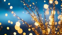 Glowing golden bokeh lights and sparkly branches against deep blue background create magical festive atmosphere for holiday celebrations and events.