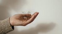 Hand holding transparent glass light bulb with visible filament against neutral background symbolizing innovation creativity and bright ideas for business concepts.