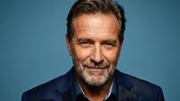 Confident mature Caucasian businessman with gray beard smiling warmly in navy suit against blue background for corporate headshot and professional marketing.