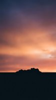 Dramatic sunset sky with vibrant orange pink purple clouds over silhouetted mountain landscape horizon for nature backgrounds and scenic designs.