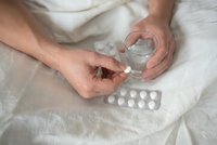 Person taking medication with water glass in bed, healthcare routine, daily medicine intake, pharmaceutical treatment concept.