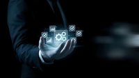 Businessman in dark suit holding glowing digital hologram with gears, checkmarks and analytics icons, representing technology solutions and business process optimization.
