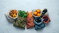 Fresh vegetables and fruits in reusable eco bags on marble surface, flat lay. Zero waste sustainable grocery shopping concept.