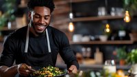 Happy African American chef presenting gourmet salad dish in modern restaurant kitchen with warm lighting for culinary marketing and food service.