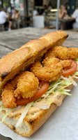 Crispy fried shrimp po boy sandwich with lettuce and tomato on crusty bread served at outdoor cafe restaurant for lunch meal.