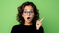 Young Hispanic woman with curly hair and glasses showing surprised expression, pointing finger up against green background. Emotional portrait for advertising.