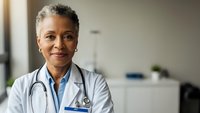 Confident African American female doctor with stethoscope smiling in modern medical office, healthcare professional portrait for medical marketing.