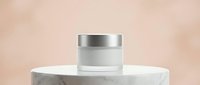 Cosmetic jar with silver lid displayed on white marble podium against neutral beige background, suitable for skincare, beauty product packaging mockups.
