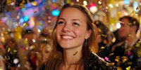 Young Caucasian woman smiling at celebration with colorful confetti falling around her, capturing joy and festive atmosphere at night event.