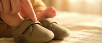 Adult hands gently putting on cozy beige slippers with velcro straps in warm sunlit room. Comfortable footwear for relaxation and home comfort.