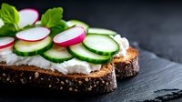 Fresh sandwich with cream cheese, sliced radish and cucumber on dark rye bread against black background. Healthy vegetarian breakfast concept.