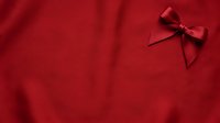 Red fabric background with decorative bow ribbon in corner, suitable for holiday greeting cards, gift wrapping designs, festive promotions, and seasonal marketing materials.