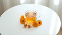 Herbal tea with dried calendula flowers on white round table, wellness and natural remedy beverage for relaxation and health.