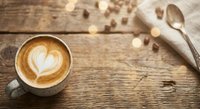 Coffee cup with heart latte art on rustic wooden table with warm bokeh lights and linen napkin creating cozy cafe atmosphere for morning beverage concepts.