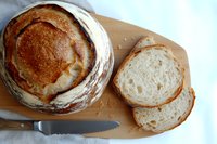 Freshly baked artisanal sourdough bread with crispy crust and airy crumb texture on wooden cutting board, sliced to show open crumb structure and served with knife.