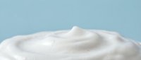 Creamy white cosmetic product with smooth swirled texture on soft blue background for skincare and beauty applications.