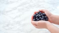 Hand holding fresh blueberries over marble surface, ideal for food, nutrition, healthy eating, and organic produce marketing materials.