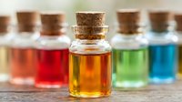 Colorful liquid samples in glass bottles with cork stoppers arranged on wooden surface, representing chemical solutions, essential oils, or laboratory experiments for scientific research and education.