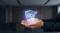 Businessman hand holding glowing digital shield with checkmark symbol representing cybersecurity protection and data safety in modern office environment.