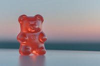 Red gummy bear candy standing alone on a surface with a soft pastel sunset background, sweet treat concept for confectionery and food design.