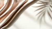 Elegant beige silk fabric with soft folds and palm leaf shadow creating minimalist luxury composition against white background. Suitable for fashion and beauty industry.