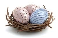 Decorative Easter eggs with metallic pattern in soft pink and blue colors resting in natural twig nest on white background, isolated seasonal composition.
