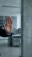 Male professional in business attire making stop gesture at glass office door, denying access to secure corporate workspace with data security signage visible inside modern office environment.