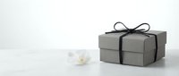 Gray gift box with black ribbon bow and white orchid flower on clean white background for elegant present packaging and celebration design.